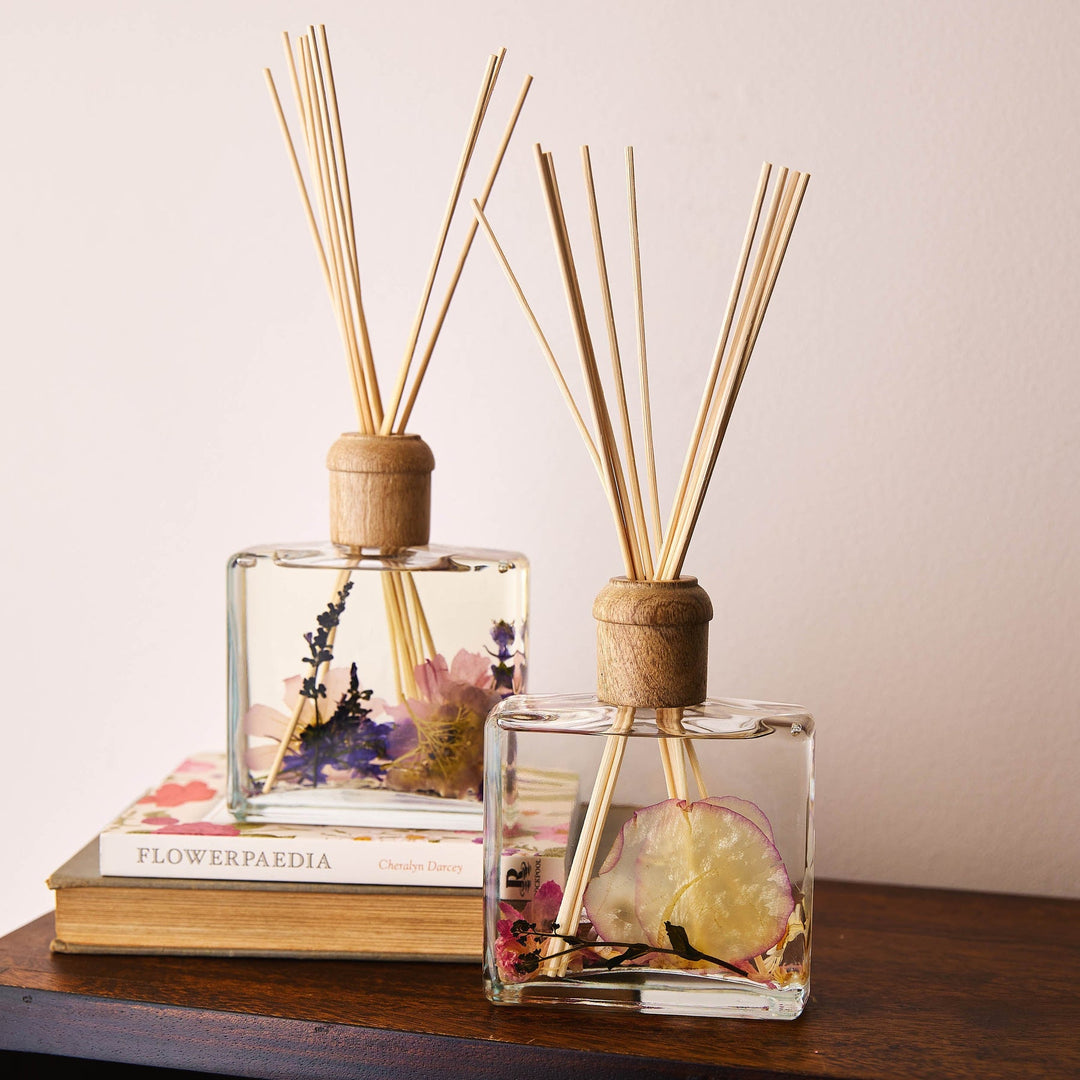 Rosy Rings Roman Lavender Scented Reed Diffuser with 10 reed sticks and wooden cap displayed on top of wooden shelf and flower books