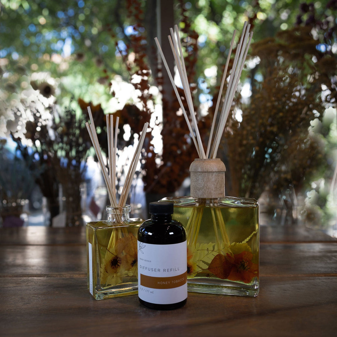 Large and Small Rosy Rings Honey Tobacco Scented Reed Diffuser displayed next to Diffuser Refill Bottle